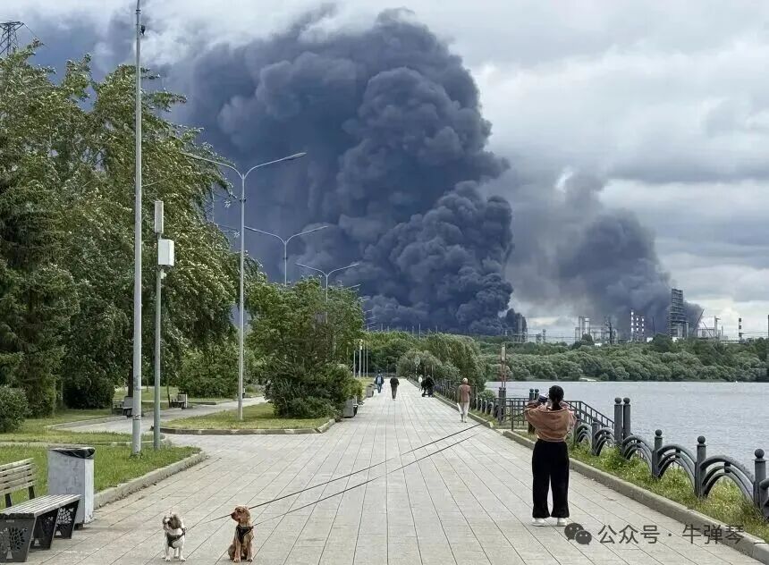 People walk in a park as black smoke rises from the area of the Russian oil producer Gazprom Neft's Moscow oil refinery on the southeastern outskirts of Moscow on June 18, 2026.